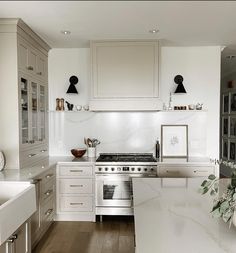 a white kitchen with marble counter tops and stainless steel appliances, along with wooden flooring