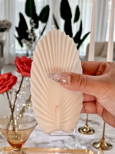 a hand holding a white shell shaped object on top of a table next to red roses