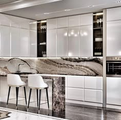 a kitchen with marble counter tops and white cabinets, along with two bar stools