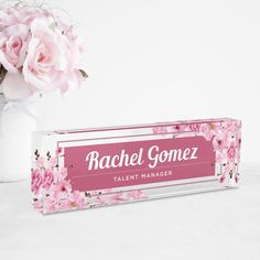 a vase filled with pink flowers sitting next to a sign that says rachel gomezz talent manager