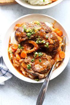 two bowls filled with meat and vegetables on top of a white tablecloth next to bread