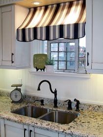 a kitchen with white cabinets and granite counter tops, black and white striped valance over the sink