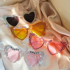 three pairs of heart shaped sunglasses with crystals on the sides and pink, orange, yellow, and blue shades