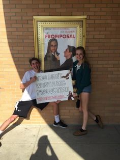 two young people holding a sign in front of a brick wall with a poster on it