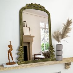 a mirror sitting on top of a mantle next to a vase with a plant in it