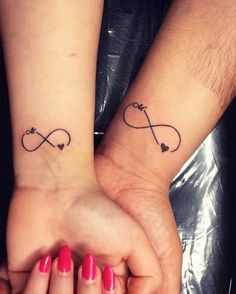 two people holding hands with tattoos on their wrists and one has a heart in the middle