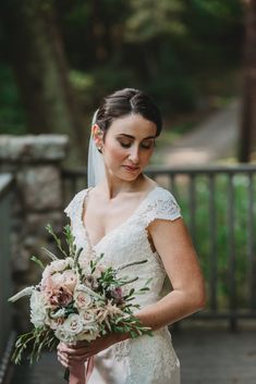 a woman in a wedding dress holding a bouquet and looking down at her face while standing on a bridge