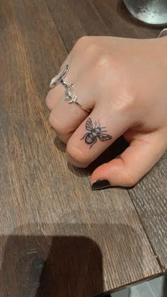 a woman's hand with a spider tattoo on her left thumb and ring resting on the table