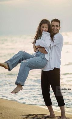 a man carrying a woman on his back while standing on the beach near the ocean