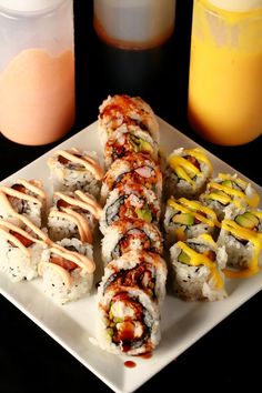 sushi rolls are arranged on a white plate next to orange juice and an orange drink