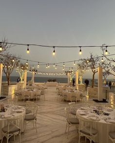 an outdoor dining area with tables, chairs and lights strung over the top of it