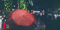 a person holding an umbrella in the rain on a city street with christmas lights behind them