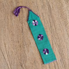 a green piece of cloth with purple flowers and tassels on it sitting on a wooden surface