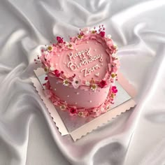 a pink birthday cake sitting on top of a white sheet