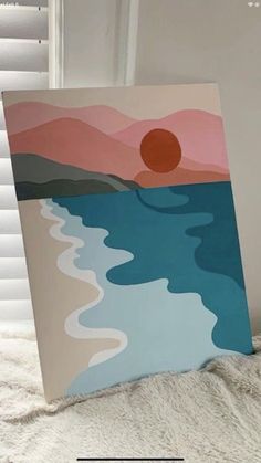 a painting is sitting on a bed next to a window with the sun in it