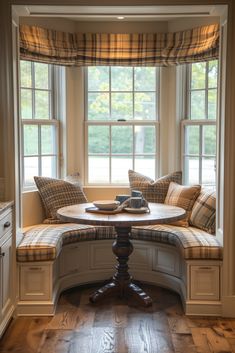 a corner window seat with pillows on it in front of a table and windowsill