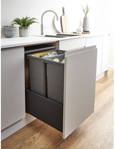 an open cabinet in the middle of a kitchen with two trash cans and a sink