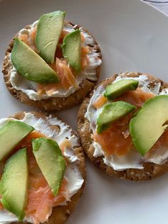 three crackers with cream cheese, salmon and avocado on them sitting on a white plate