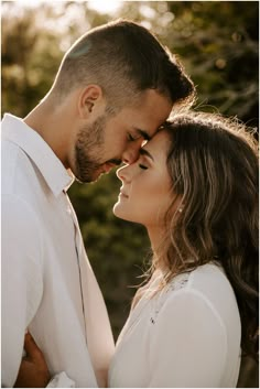 a man and woman standing next to each other in front of trees with the sun shining on them