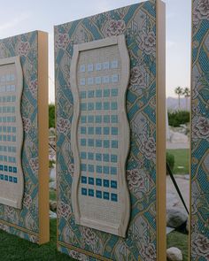 two decorative panels on the side of a building with grass and rocks in front of them