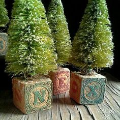 three small trees are sitting in blocks on a wooden table with letters painted on them