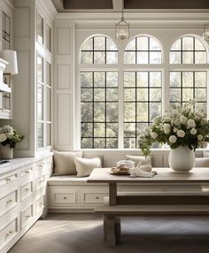 a table with flowers in a vase on top of it next to a bench and windows