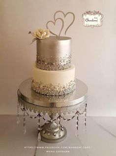 a three tiered cake with two hearts on top is sitting on a silver platter