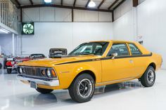 an old yellow car in a garage with other cars behind it and a clock on the wall