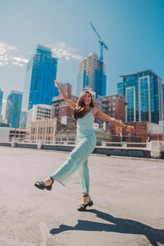 a woman is dancing in the middle of an empty parking lot with skyscrapers in the background