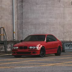 a red car parked in front of a building with graffiti on the wall behind it