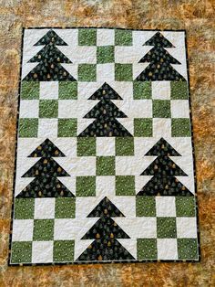 a green and white quilt with black trees on it's side, sitting on a brown surface