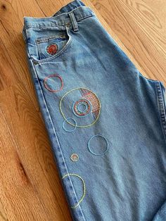 an old pair of jeans with embroidered circles on them sitting on the floor in front of a wooden floor