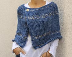 a woman standing next to a wall wearing a blue knitted sweater and white shirt