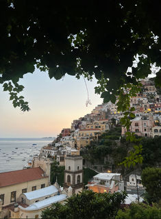 a view of some buildings and the ocean in the distance from a hill side town