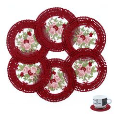 four red doily with pink flowers and green leaves on them next to a cup