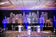 a stage set up with chairs and tables in front of a cityscape backdrop