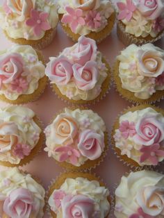 cupcakes with pink and white frosting roses on them are arranged in rows