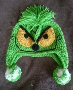 a crocheted hat with an angry grin face on the front and green hair