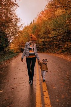 a woman and child walking down the road in the fall with leaves on the ground