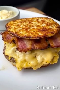 a bacon and cheese sandwich on a white plate with a small bowl of mayonnaise