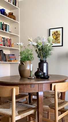 two vases with flowers sit on top of a table in front of bookshelves