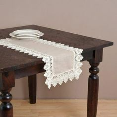 a wooden table topped with a white plate and a lace covered placemat on top of it