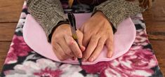 a woman sitting on top of a pink flower covered floor with a pen in her hand