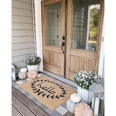 a welcome mat on the front porch with pumpkins and flowers in vases next to it