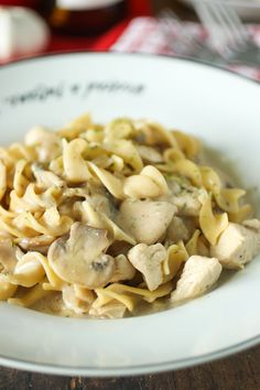 a white plate topped with pasta covered in mushrooms and sauce on top of a wooden table