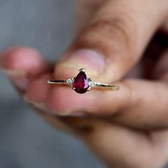 a person holding a ring with a red stone in it's middle and two white diamonds on the other side