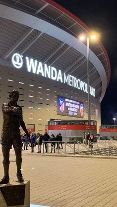 a statue in front of a stadium with people walking around the area at night time