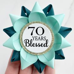 a close up of a person's hand holding a brooch with the words 70 years blessed on it