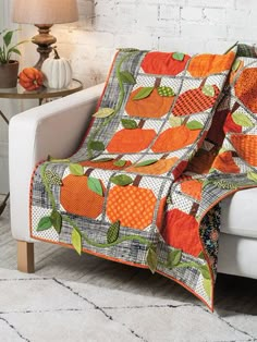 an orange quilt on a white couch in a living room with a table and chair