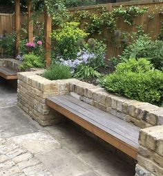 a wooden bench sitting in the middle of a garden next to a stone wall and flowers